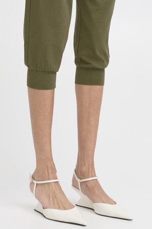 Bas des jambes portant un pantalon court vert olive et des escarpins compensés blancs à bout pointu avec bride à la cheville.