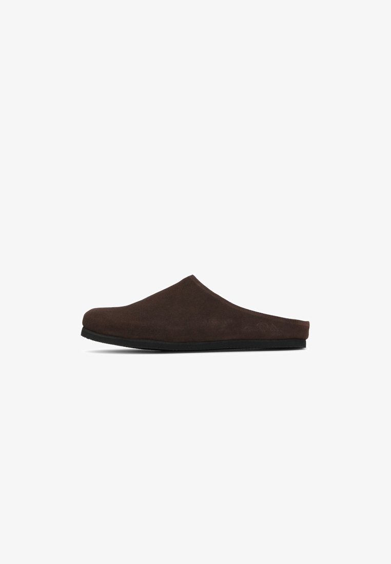 Chausson en daim marron à enfiler avec un devant arrondi, un profil bas et une surface texturée. Semelle en caoutchouc noir offrant une bonne adhérence. Aucun logo ou accent visible.