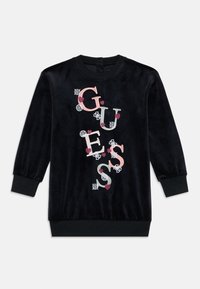 Crna dugačka haljina s dugim rukavima od baršuna s rebrastim manžetama i rubom, koja ima ružičaste i bijele izvezene natpise "GUESS" s detaljima srca i cvijeta.