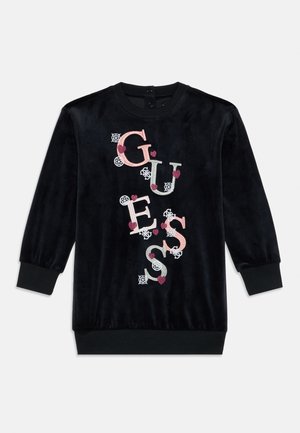 Abito lungo in velluto nero con maniche lunghe e polsini e orlo a coste, decorato con lettere ricamate in rosa e bianco che formano la scritta "GUESS", con dettagli a forma di cuore e fiore.