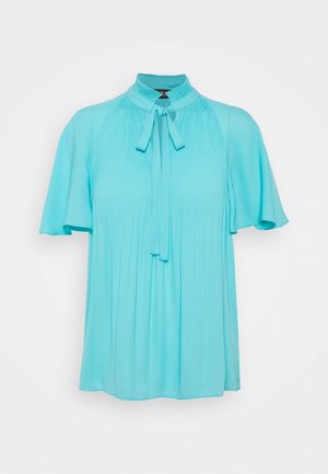 Turkos blus med korta, fladdrande ärmar, veckad fram, hög nacke med knytdetalj och mjukt, flödande tyg.