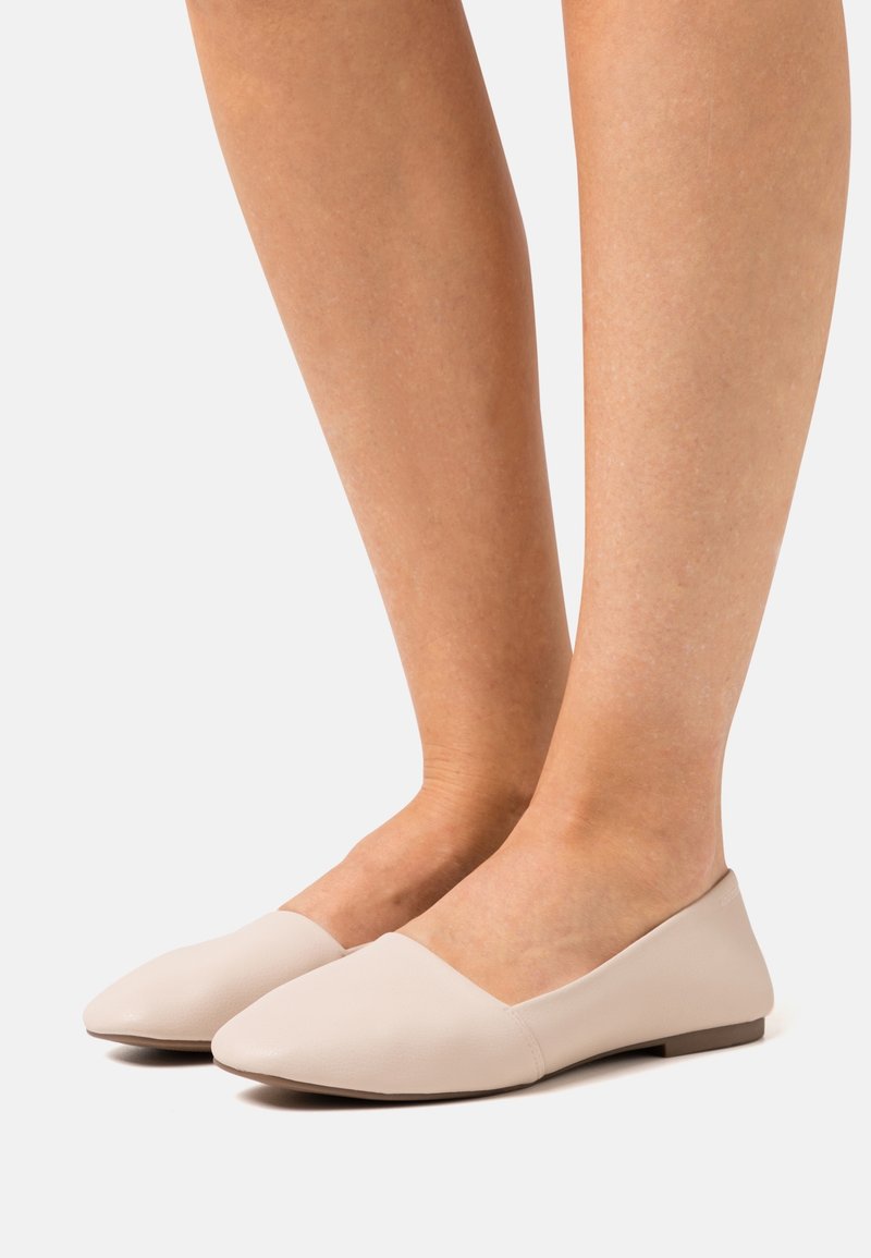 Ballerines beiges en matériau synthétique texturé avec un bout pointu et un talon bas et plat, présentant un design minimaliste et des lignes épurées.
