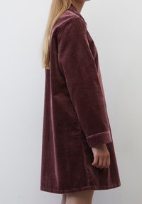 Violetti corduroy-mekko, jossa on pitkät hihat, rento leikkaus ja kaulus. Pinnassa on ribbatty rakenne, ja helma päättyy reiden keskikohtaan.