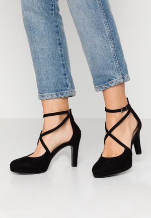 Černé semišové lodičky na vysokém podpatku s křížovými řemínky, kulatou špičkou a hladkým povrchem. V kombinaci s ohrnutými světle modrými džíny.