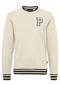 Krémová mikina s žebrovaným černobílým lemem a manžetami. Na hrudi je vyšívané písmeno "P". Celkově má měkkou texturu.