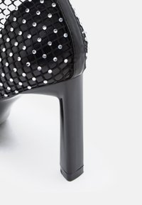 Μαύρο παπούτσι με ψηλό τακούνι, με επάνω μέρος από δίχτυ και ασημένια τρουκ, χοντρό τακούνι, λεία υφή και κομψό μυτερό σχέδιο.