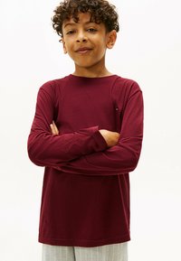 Bordeauxrotes Langarmshirt aus weichem Stoff; hat einen Rundhalsausschnitt, gerade Schnittform und ein kleines Logodetail auf der Brust.