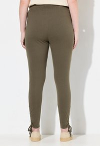 Olivgröna stretchleggings med en figurnära design, samlade anklar och en slät yta. Elastisk midja för komfort.
