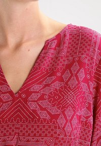 Top de cuello en V de tissu rosa brillante con intrincados patrones geométricos y puntos blancos. Textura suave con mangas cortas.
