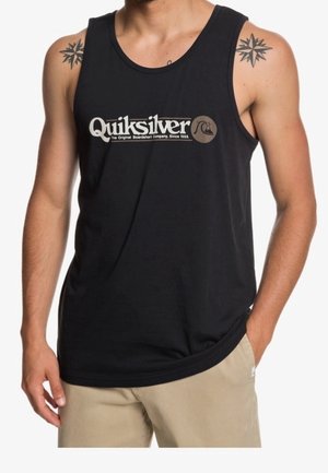 Mann trägt ein schwarzes Quiksilver-Ärmelloses Shirt mit beigefarbenen Shorts, zeigt Stern-Tattoos auf beiden Schultern, die Arme entspannt seitlich hängend.
