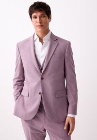 Completo color lavanda con taglio su misura, design monopetto, rever a incavo, due tasche frontali e bottoni marroni; abbinato a una camicia bianca.