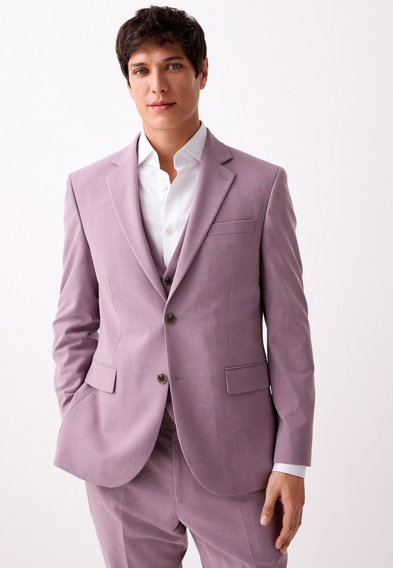 Completo color lavanda con taglio su misura, design monopetto, rever a incavo, due tasche frontali e bottoni marroni; abbinato a una camicia bianca.