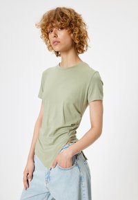 Lys grøn kortærmet t-shirt med rund halsudskæring, blødt bomuldsstof og skrå sidelommer. Båret med løstsiddende lyseblå jeans.
