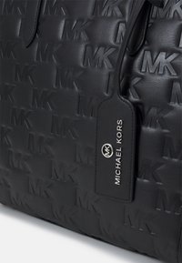 Zwarte leren tote bag met reliëfpatroon van het "MK"-logo, voorzien van een rechthoekig label met "MICHAEL KORS" gegraveerd, met een gladde textuur.