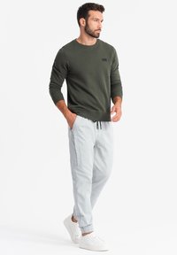 Sudadera de color verde oliva con cuello redondo y un discreto parche de logo, combinada con pantalones jogger gris claro con bolsillos laterales y dobladillos ajustados.