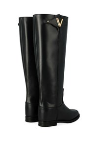 Une paire de bottes noires en cuir hautes avec des talons bas et un détail doré en forme de "V" près du haut sur fond blanc.