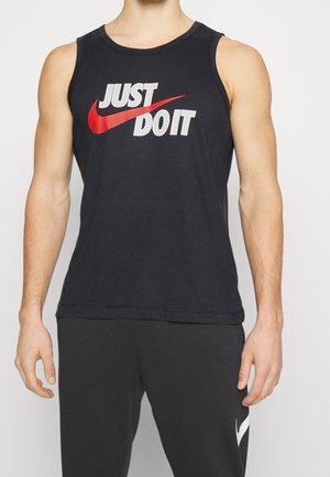 Torso masculino con una camiseta sin mangas negra que lleva el texto "JUST DO IT" y el logo de Nike en rojo, combinado con pantalones negros de Nike.