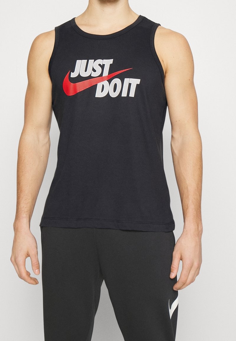 Mannelijk bovenlijf gekleed in een zwarte mouwloze shirt met de tekst "JUST DO IT" en het rode Nike swoosh-logo, gecombineerd met zwarte Nike-broek.