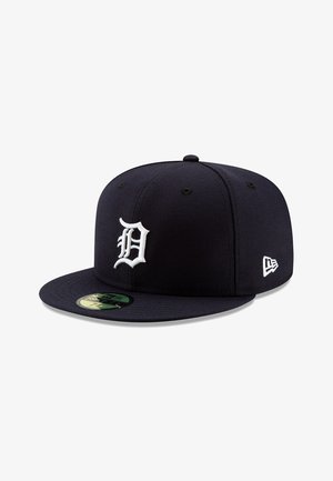 Gorra de béisbol azul marino con visera plana, que presenta un logotipo "D" bordado en blanco en relieve en la parte frontal y un logotipo pequeño en el lateral, fabricada en tela.