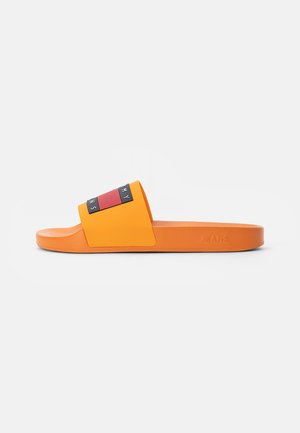 Sandale orange à enfiler avec une large bride comportant un logo rectangulaire rouge et noir et « USANS » embossé sur la semelle latérale.