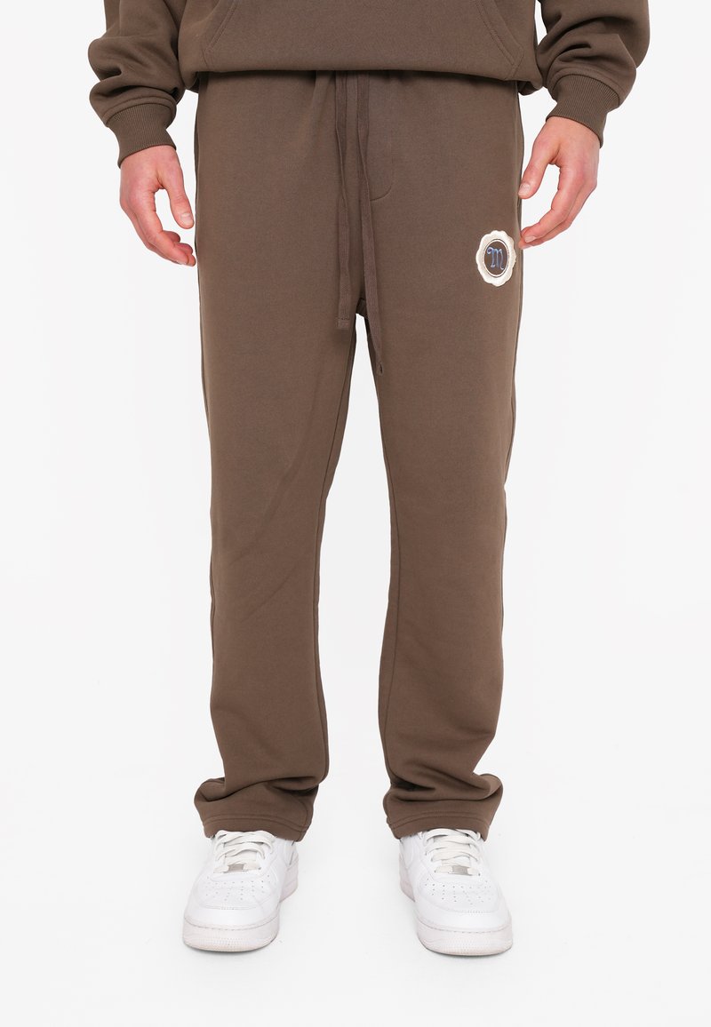 Braune Baumwoll-Sweatpants mit verstellbarem Bund und Seitentaschen, mit einem runden Logopatch am linken Oberschenkel.