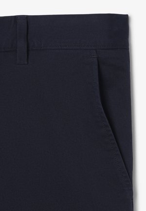 Primer plano de pantalones azul marino oscuro que muestran la pretina, trabilla para cinturón y bolsillo lateral inclinado con costuras visibles.