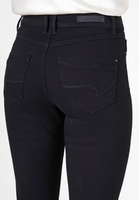 Schwarze Jeans aus Denim im Slim Fit, mit dezenten Nähdetails an den hinteren Taschen und einer glatten Textur. Etikett am Bund sichtbar.