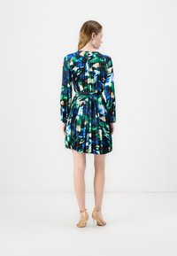 Vestido curto plissado em azul, verde e padrão abstrato em creme. Mangas longas, decote redondo e uma cintura bem definida com um cinto a condizer.