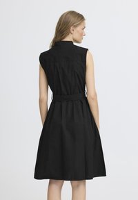 Vestito nero senza maniche con colletto, cintura in tessuto e gonna a campana. Presenta un design pulito e una texture liscia.