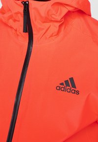 Bright orange waterproof jacket with a black zipper, adjustable hood, and black Adidas logo on the left chest area. Smooth texture.