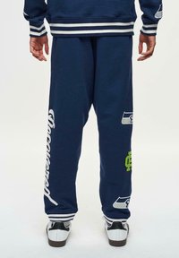 Marineblauwe sweatpants met witte accenten en logo's, met een comfortabele pasvorm, geribbelde boorden en een zachte textuur.