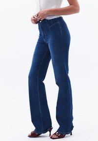 Högmidjade blå denimjeans med utsvängda ben, som har kontrasterande sömmar och en tvåknappsknäppning i midjan.