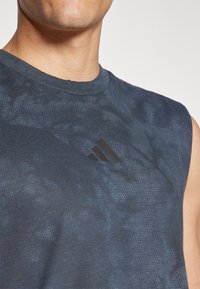 Mornarsko plava bezrukava sportska majica s teksturiranom tkaninom. Sadrži crni Adidas logo na prsima. Gladak izrez oko vrata, anatomski kroj.