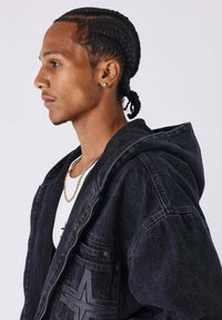 Zwarte denim hoodie met trekkoordkap, voorzien van een grote voorzak en geborduurd ontwerp; gedragen over een wit shirt met een gouden ketting.