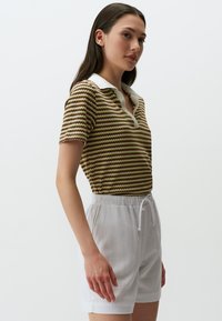 Maglietta polo in maglia con motivo zigzag verde e marrone, colletto bianco, abbinata a pantaloni corti bianchi con coulisse, caratterizzata da una vestibilità comoda e una texture morbida.