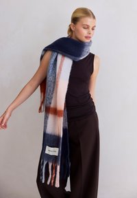 Écharpe en mélange de laine bleu marine, gris et pêche avec un motif à carreaux, des extrémités frangées, et une étiquette portant l'inscription "Arctic Fox" près de la base.