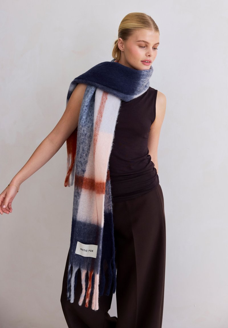 Écharpe en mélange de laine bleu marine, gris et pêche avec un motif à carreaux, des extrémités frangées, et une étiquette portant l'inscription "Arctic Fox" près de la base.