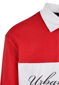 Tricou polo roșu și alb, cu o secțiune superioară roșie solidă, o secțiune inferioară albă și guler cu detalii în scris negru.