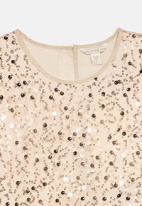 Μπεζ φόρεμα με στρογγυλή λαιμόκοψη, διακοσμημένο με ποικιλία μεγεθών παγιέτες σε ασημί και μαύρο, που δημιουργούν ένα κυματιστό μοτίβο στον ύφασμα.