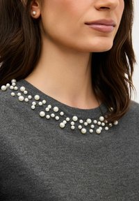 Šedý svetr s kulatým výstřihem zdobeným perleťovými ozdobami různých velikostí kolem límce. Hladká textura.