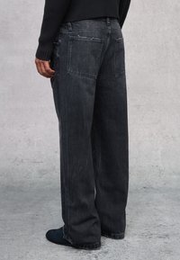 Jeans de pierna ancha de color gris oscuro, confeccionados en denim, con un corte relajado, dos bolsillos traseros y una textura ligeramente desgastada a lo largo de las costuras.