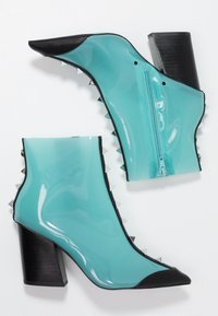 Bottines en plastique aqua avec accents noirs, dotées d'une fermeture éclair et de détails en pointes métalliques sur les côtés, talons carrés et bouts pointus.