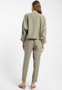 Oliwkowy, luźny zestaw składający się z dwóch części, składający się z krótkiego topu z zaokrąglonym tyłem i spodni z wysokim stanem o tapered kroju. Gładka tekstura, minimalny design.