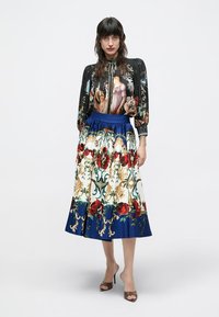 Blouse à manches longues avec un fond sombre et des figures peintes colorées. Jupe maxi à motif floral avec une ceinture et un ourlet bleus.