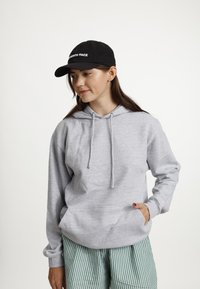 Grijze hoodie met een voorkantzak en trekkoorden. Gecombineerd met groen-witte gestreepte broek. Zwarte pet met witte tekst.