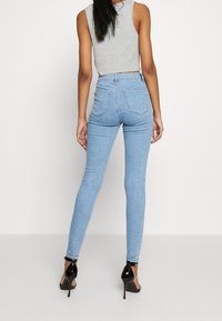 Jeans ajustados de un azul claro, hechos de denim, con cintura alta, bolsillos traseros y una textura suave. Llevados con tacones de aguja negros.