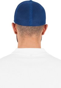 Șapca albastră din plasă are un design structurat, cu un bor flat. Persoana are părul scurt și poartă un tricou polo alb.
