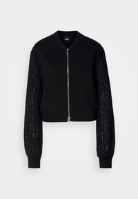Lyhyeksi leikattu musta neulecardigan, jossa on tasainen vartalo, ribbireunus kauluksessa ja tekstuuripinta hihoissa. Varustettu vetoketjukiinnityksellä edessä ja joustinsuojilla.