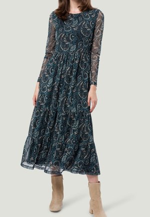 Długa sukienka maxi z długim rękawem w kolorze morskim z wzorem paisley. Przezroczyste rękawy i marszczona talia dodają objętości. Dobrana do beżowych botków za kostkę.