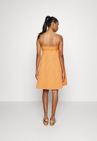 Vestido laranja de alças com tecido texturizado, corpete ajustado e saia em linha A. Apresenta um fecho nas costas e comprimento até à metade da coxa.